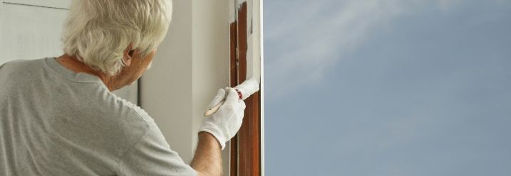 Mann streicht Holzfenster weiß